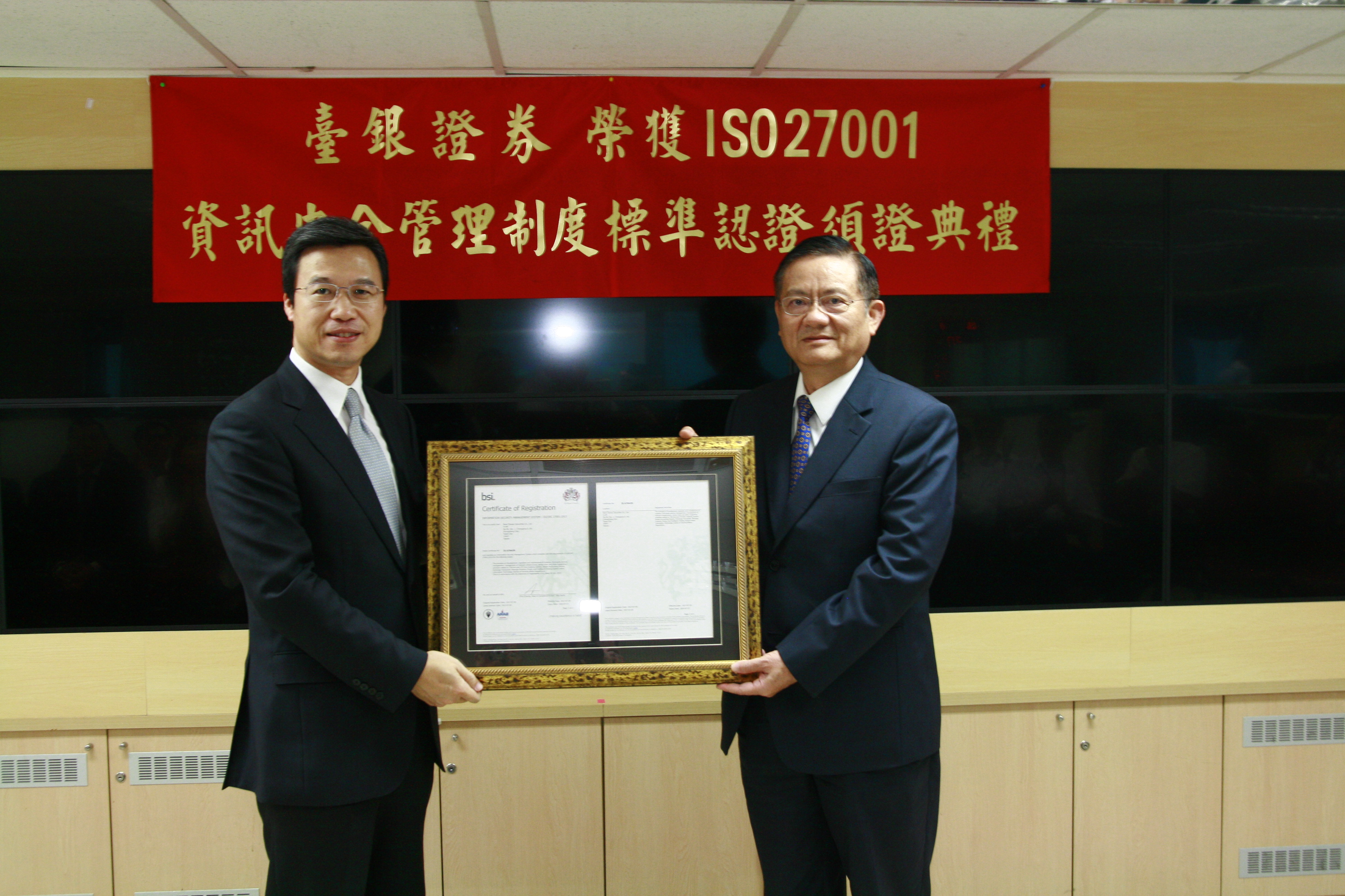 臺銀證券總經理江士田(右)，接受ISO27001驗證單位英國標準協會(簡稱「BSI」)台灣分公司總經理蒲樹盛(左)頒發證書之照片